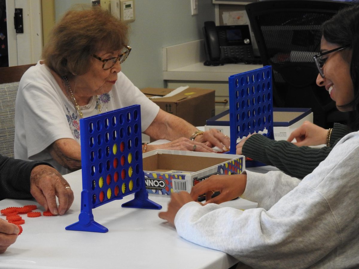Senior Meshva Patel plays "Connect Four" with a retirement home resident.